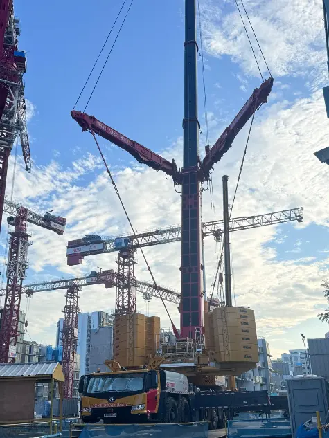 Large luffing mobile crane lifting a PPVC module beside residential towers