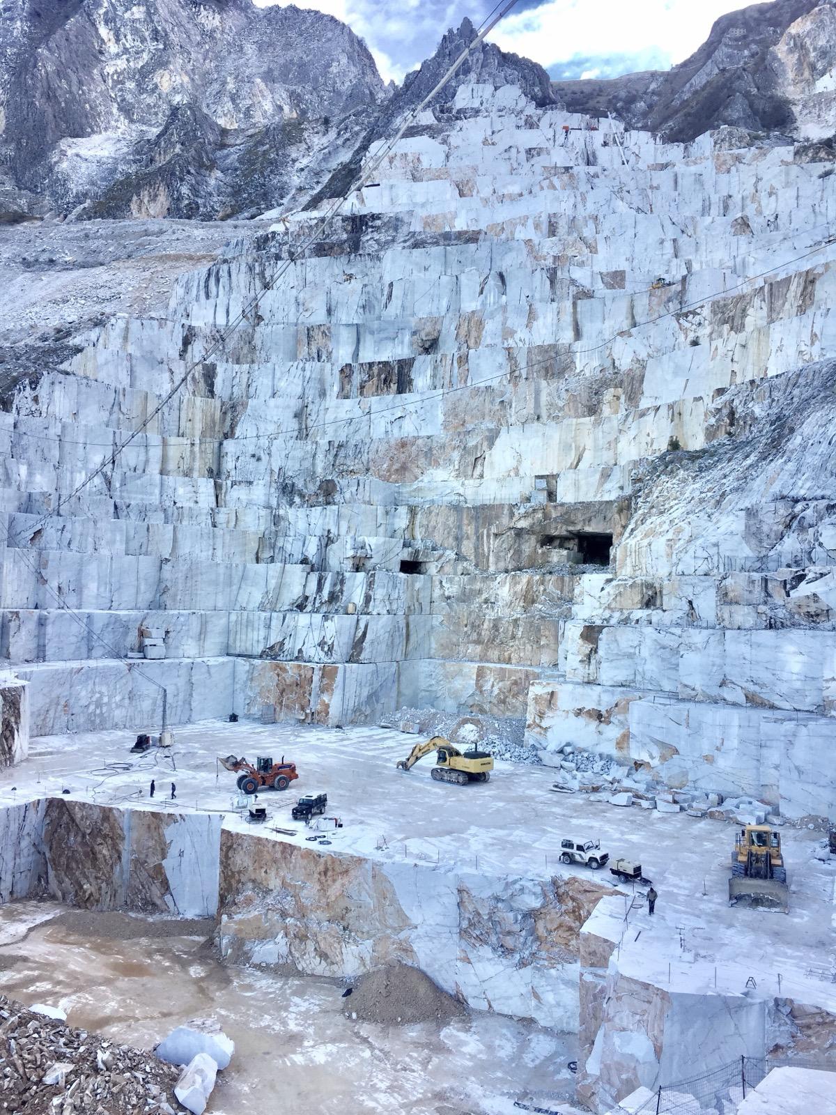 Carrara marble quarry cut into white terraces with excavators working below